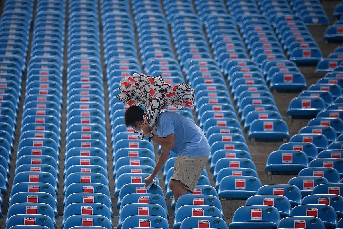 Far left: A worker uses a stack of stickers as an "umbrella" to shield himself from the afternoon heat as he goes about removing them from the seats. Left: A member of the cleaning crew, Mr Zarak Khan (in bright green top), 61, holds a trash bag open