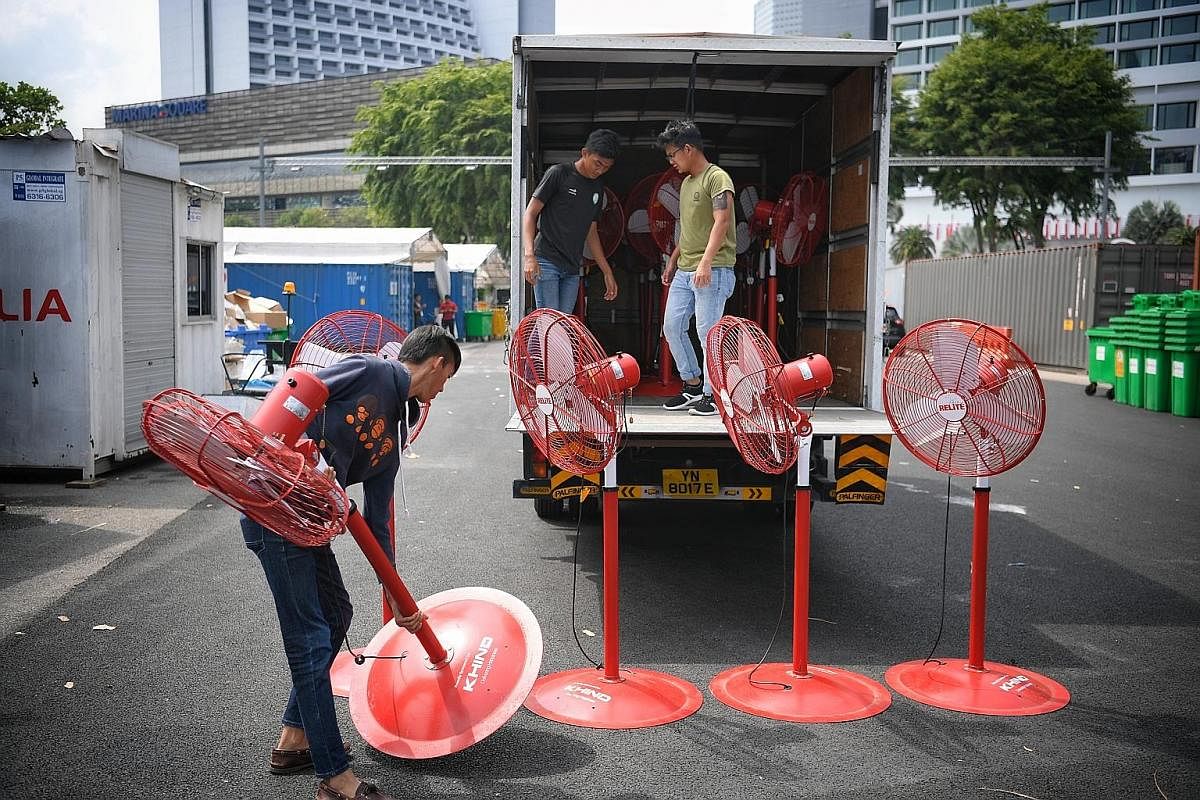 Far left: A worker uses a stack of stickers as an "umbrella" to shield himself from the afternoon heat as he goes about removing them from the seats. Left: A member of the cleaning crew, Mr Zarak Khan (in bright green top), 61, holds a trash bag open