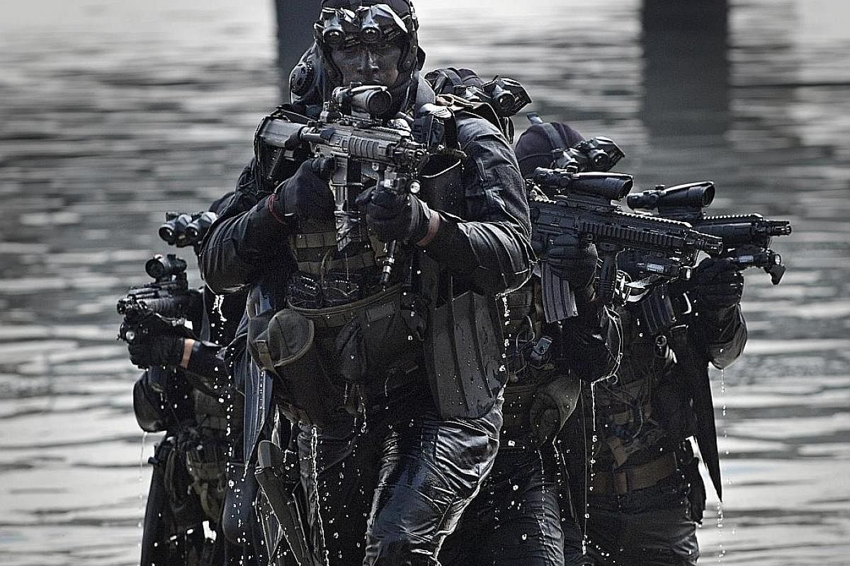 Clothed in black for stealth and carrying highly accurate and rugged Heckler & Koch HK416 assault rifles, a team of naval combat divers emerge from the water during a demonstration of their "over-the-beach" capabilities. With weapons ready to engage 
