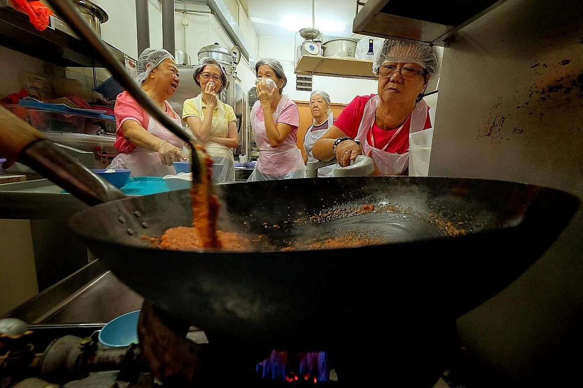 Trainees (from left) Hoo Jan Wah, 77, Tan Soi Noi, 60, Ng Siew Tim, 60, Heng Tang Kwee, 69, and Chia See Moy, 68, watch intently as Mr Wang (not in photo) stirs assam paste in the wok. Some of them cover their faces with cloth as the chilli from the 