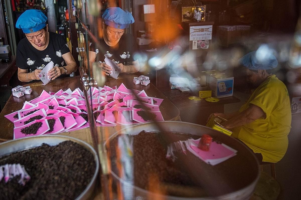 Pek Sin Choon employee Peh Bee Leng (in black), 78, wraps blended tea leaves in paper packets the traditional way, while Madam Lim Boh Tan (in yellow), 82, packs them into a tin container. Both women are Mr Kenry Peh's aunts, and Madam Lim is the company'