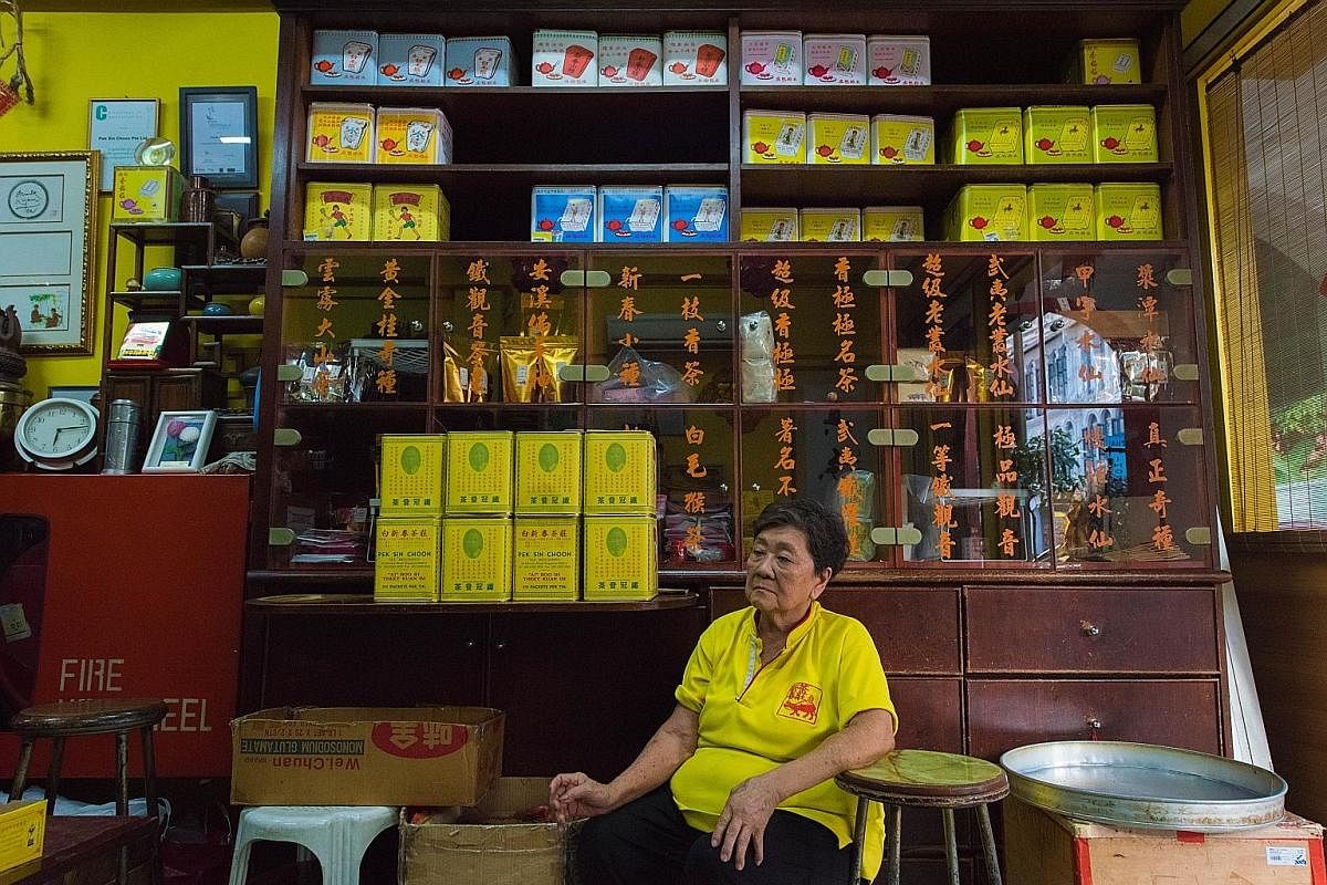 Madam Lim Boh Tan takes a break after a day's worth of work wrapping tea packs. The Chinese characters written in orange on the cupboard behind her are the names of traditional house blends, some of which have been discontinued.