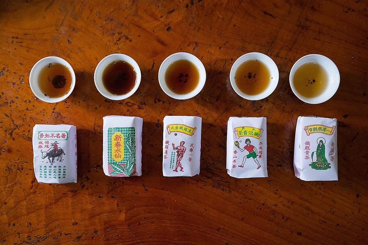 Cups of tea with brews in different shades of brown are lined up against various packets of tea with designs that include a juggler and a girl playing ping pong.