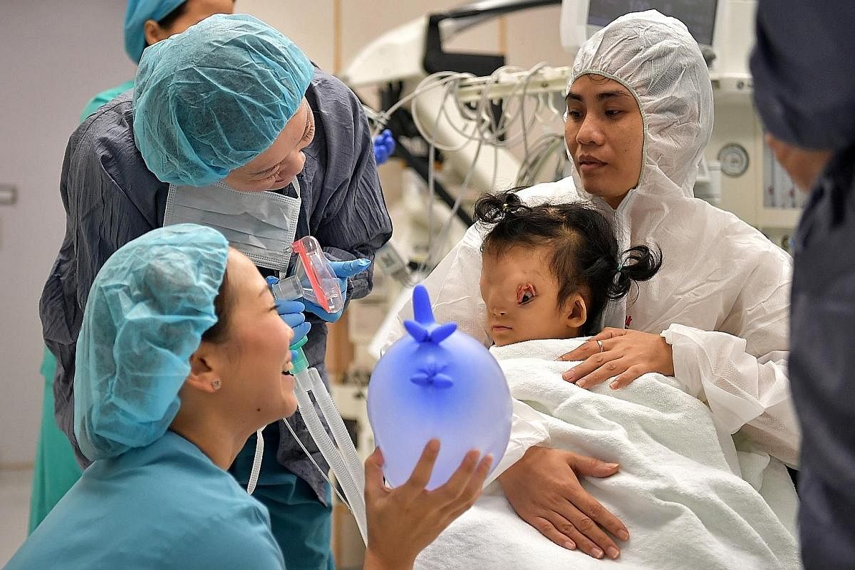 Mount Elizabeth Hospital staff cheering Ton Nu Hoang Dung before she was put under general anaesthesia for an operation last month. Her mother, Madam Hoang Thi Thuy Linh, is carrying her on her lap. Above left: Madam Mai Thi Thien Thanh, 35, and her 
