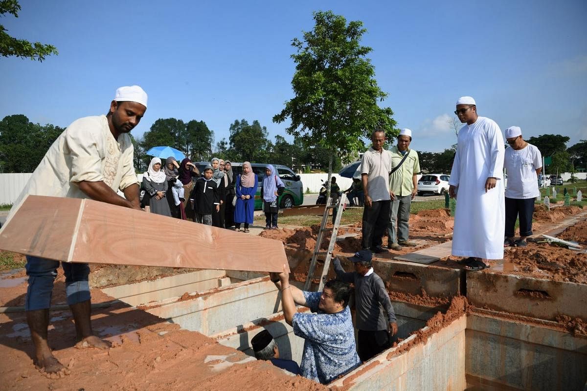 Undertaker Muhammad Razaly Osman (second from right) and participants in the Jenazah Management Course watch workers lift a wooden plank casing called papan long into a grave to be placed over the body during a burial at the Pusara Aman Cemetery in Lim Ch