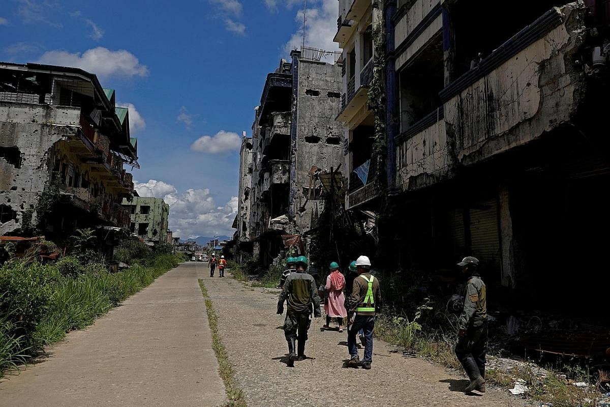 Internally displaced people walking with safety managers during a visit to the war-torn area of Marawi City last month. They have to agree to have their wrecked homes demolished before rebuilding can start. An evacuation camp in Marawi City. The gove