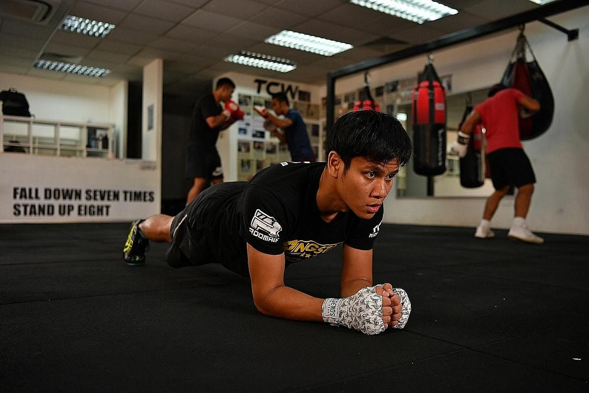 Ridhwan doing planking exercises, which improve the core muscles and stability. Inspirational messages such as "Fall down seven times, stand up eight" are painted on the walls of the gym.
