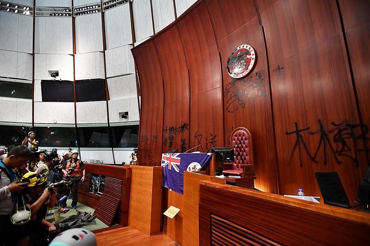 Left: A protester trying to smash a glass door at the Legislative Council (LegCo) building in Hong Kong yesterday. Above: Protesters put a British colonial-era flag on the LegCo chamber's podium and spray black paint on the Hong Kong bauhinia emblem 