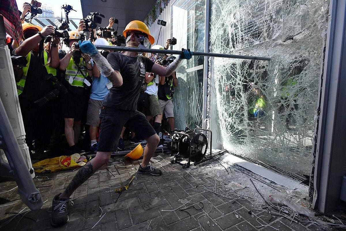 Left: A protester trying to smash a glass door at the Legislative Council (LegCo) building in Hong Kong yesterday. Above: Protesters put a British colonial-era flag on the LegCo chamber's podium and spray black paint on the Hong Kong bauhinia emblem 