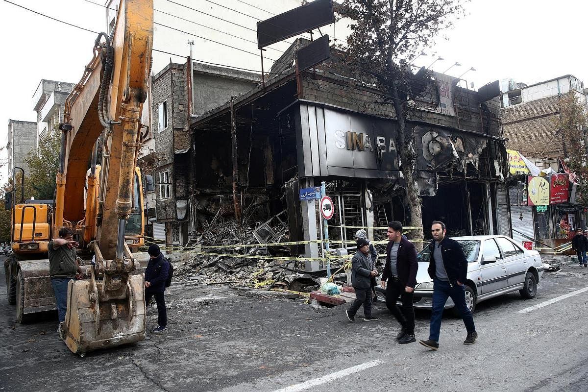 A bank damaged by fire in Teheran after protests on Nov 20. The authorities have arrested dozens and restricted Internet access. Iranians looking at the wreckage of a bus that was set ablaze by protesters during a demonstration in the central city of