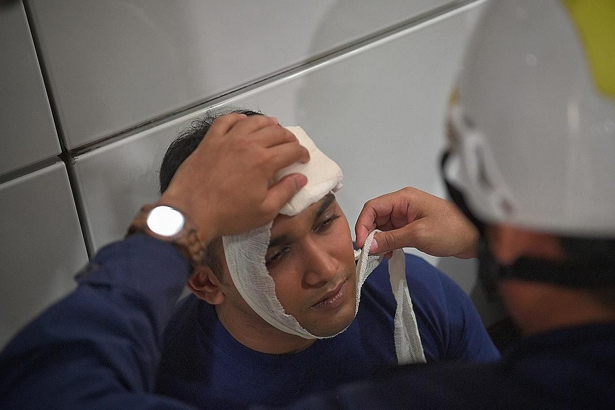 An exercise participant with a simulated head injury being bandaged up by a PSRU serviceman at a first-aid point.