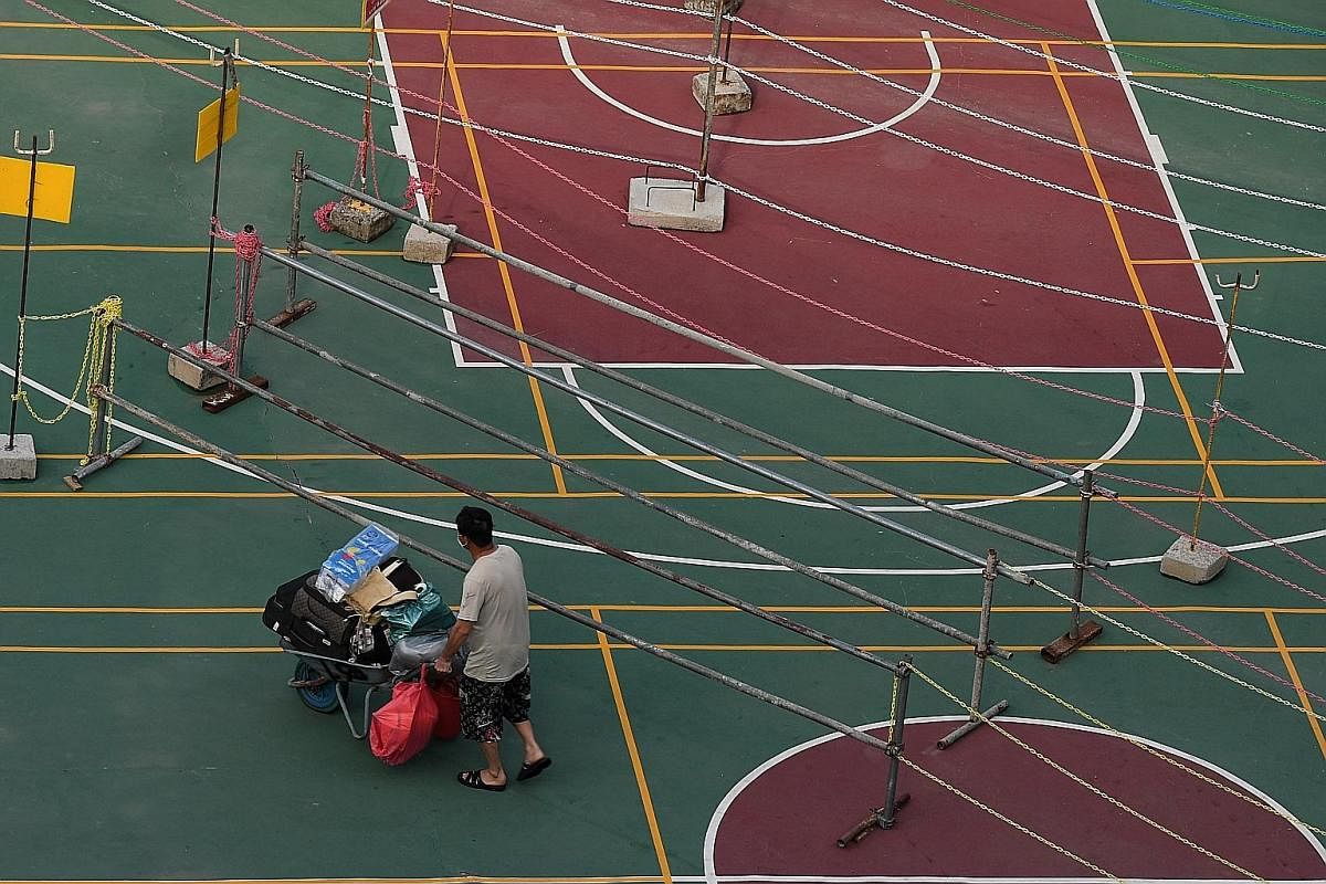 A foreign worker walking past aisles marked out by metal poles and chains strung across a basketball court at an on-site dormitory at a Kim Keat Avenue worksite on Aug 19. As of that day, all dormitories were declared to be clear of Covid-19, includi